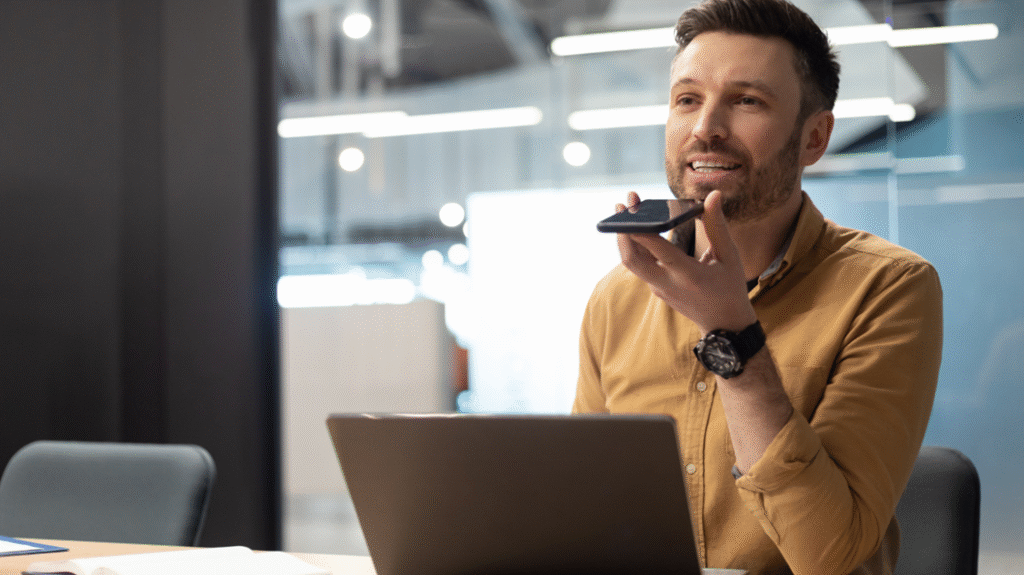 Mann sitzt am Schreibtisch und nutzt einen KI-Sprachassistenten
